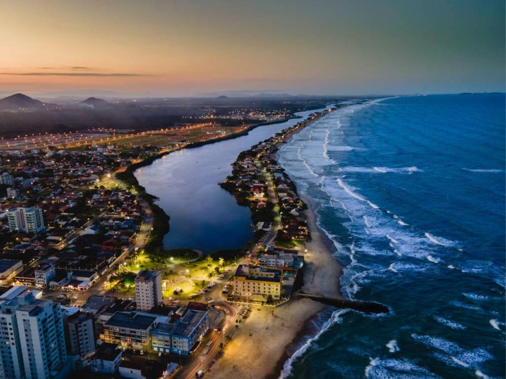 Imagem da lagoa e orla ao entardecer em Barra Velha: Vista aérea de um dos pontos turísticos de Barra Velha SC, destacando a lagoa e a orla ao entardecer. Foto: Prefeitura de Barra Velha.