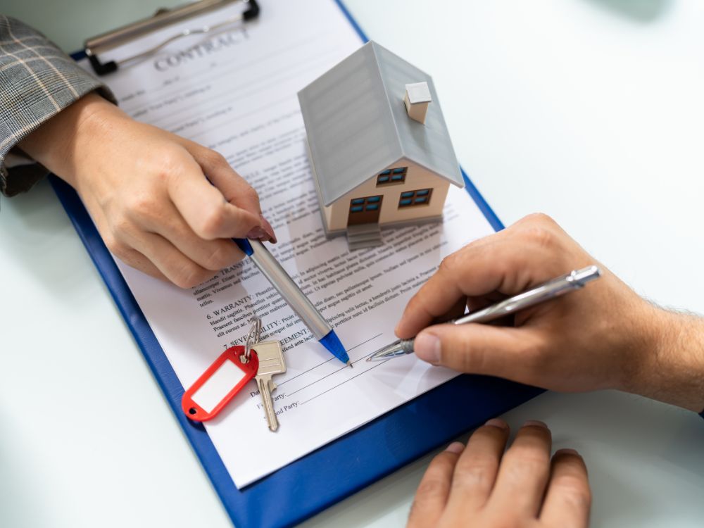 Assinatura de contrato de compra e venda de imóvel com miniatura de casa ao lado, ilustrando o processo de solicitação do desconto cartório primeiro imóvel.